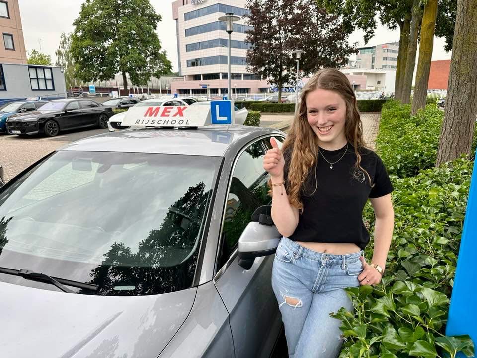 Geslaagde leerling van Rijschool MEX naast een zilveren lesauto
